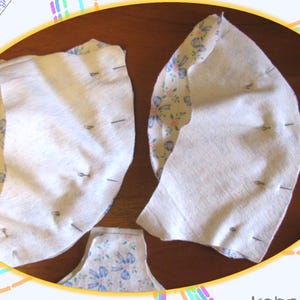 May include: Two pieces of white fabric with floral patterned fabric on the back are pinned together. The fabric is pinned along the curved edge.
