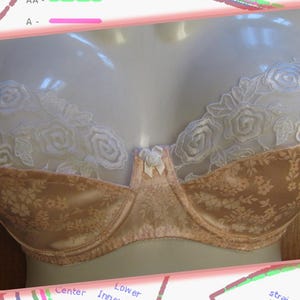 May include: A beige bra with white lace trim and floral pattern. The bra has a bow in the center and adjustable straps.