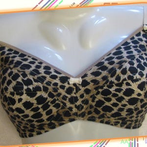 Puede incluir: Un sujetador de color marrón y negro con estampado de leopardo y un lazo blanco en el centro. El sujetador tiene tirantes ajustables.