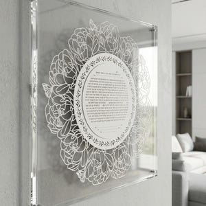 May include: Clear acrylic wall art featuring a white floral design surrounding a circular text. The text is in a script font. The artwork is mounted on a wall with silver hardware. The overall aesthetic is modern and elegant.