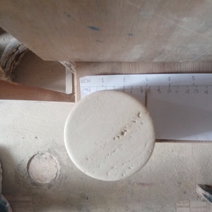 May include: A close-up of a white ceramic cylinder with a rough texture. The cylinder is sitting on a white surface with a ruler marked in inches and centimeters.