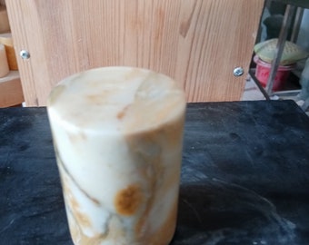 May include: A cylindrical object with a creamy white and brown marbled pattern. The object is standing on a dark surface, with a wooden background.