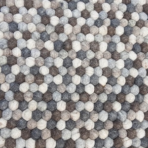 May include: A close-up of a gray, brown, and white wool rug made of small, round balls arranged in a hexagonal pattern.