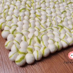 May include: A white and green wool rug made of pom poms. The rug has a textured surface and is made of 100% wool.