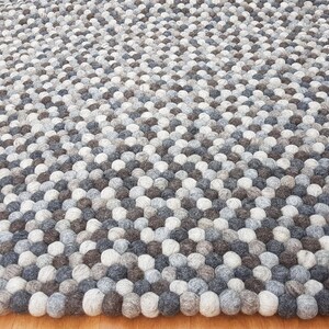 以下が含まれることがあります： グレー、ブラウン、ホワイトのウール製のフェルトボールで作られたラグ。ラグは、ダイヤモンド型のフェルトボールのパターンで構成されています。