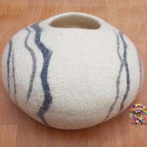 Op de afbeelding: Rond kattenbed van wit vilt met een gat om in te gaan. Het bed heeft een grijs en blauw gestreept patroon.