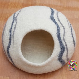 Op de afbeelding: Witte vilt kattenbed met grijze en donkergrijze strepen. Het bed heeft een ronde opening waar de kat in kan.