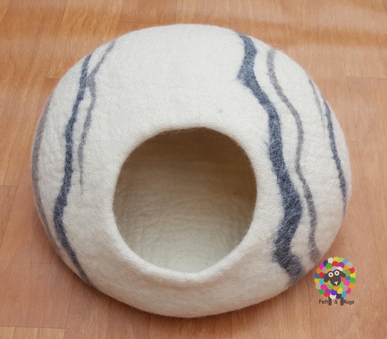 Op de afbeelding: Witte vilt kattenbed met grijze en donkergrijze strepen. Het bed heeft een ronde opening waar de kat in kan.