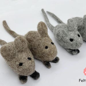 Puede incluir: Tres juguetes de ratón de fieltro con colas largas. Dos son marrones y uno es gris. Los ratones tienen ojos y narices negros.