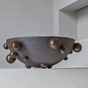 May include: A dark brown ceramic bowl with a textured surface and a unique design featuring numerous small, round, brown protrusions.