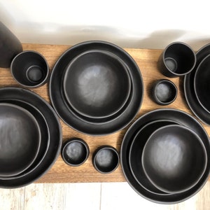 May include: A set of black ceramic bowls and plates of varying sizes. The bowls and plates have a textured, matte finish.