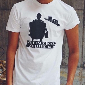 K&ouml;nnte beinhalten: Wei&szlig;es T-Shirt mit schwarzer Grafik einer Person, die in einem Stuhl sitzt, mit B&uuml;chern und dem Text "So many books, so little time". Das Shirt besteht aus weichem Material und hat kurze &Auml;rmel.