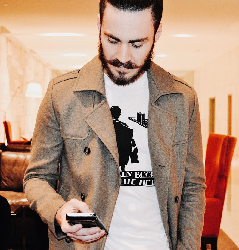 K&ouml;nnte beinhalten: Ein grauer, zweireihiger Mantel &uuml;ber einem wei&szlig;en T-Shirt mit schwarzer Grafik. Das T-Shirt zeigt eine Silhouette einer Person und den Text "MY BOOK LITTLE TIME". Die Person h&auml;lt ein schwarzes Telefon.