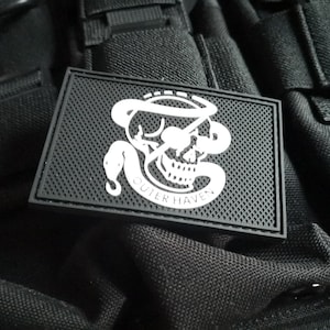 Op de afbeelding: Witte patch met een schedel en slang ontwerp. De tekst "Outer Haven" staat onder de schedel. De patch is op een zwarte achtergrond.