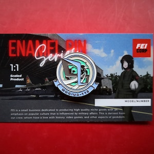 May include: A blue and white enamel pin with a stylized logo of a plane and the text "MOBIUS-118". The pin is on a card with the text "ENAMEL PIN Series" and "FEI CORP".