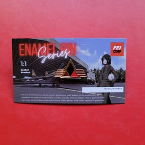 May include: A gold, black, and red enamel pin featuring a stylized triangle with the text "ENA Series" and "FEI CORP" on a white card with a background image of a plane and a woman in a military uniform.