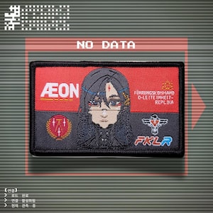 Peut inclure: Un écusson rectangulaire avec un fond rouge et une bordure noire. L'écusson présente un personnage d'anime stylisé, le texte "AEON", et le texte "FÜHRUNGSKOMHAND O-LETTE INHEIT-REPLIKA" et "FKLR".
