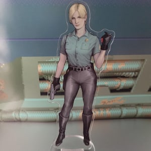 May include: A clear acrylic figure of a woman in a teal short-sleeved uniform shirt, gray pants, and black boots. She holds a gun in one hand and wears black gloves. The figure has blonde hair and a serious expression.