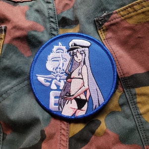 Może przedstawiać: Naszywka haftowana na niebiesko z białym statkiem, kobietą w bikini i napisem "ENEMY" w kolorze białym.