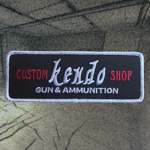 May include: White embroidered patch with black background. The text reads "CUSTOM Kendo SHOP GUN & AMMUNITION".