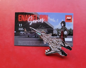 May include: A silver and black enamel pin of a fighter jet with a red tail. The pin is 1:1 scaled and features the text "ENA Series" and "FEI CORP".