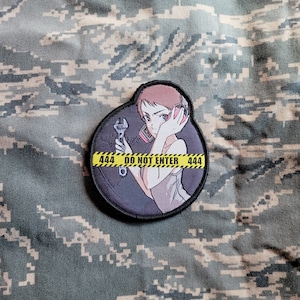 Könnte beinhalten: Ein gestickter schwarzer und weißer Aufnäher mit einer Comic-Frau, die einen Schraubenschlüssel hält. Die Frau trägt Kopfhörer und ein weißes Hemd. Der Aufnäher hat ein gelbes Warnband mit dem Text "444 BETRETEN VERBOTEN 444" drumherum.