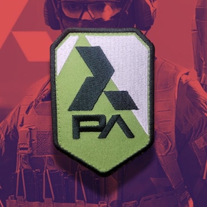May include: A shield-shaped embroidered patch featuring a split design of light green and white. The patch displays a bold black geometric logo at the top and the black letters PA positioned below, all enclosed within a thick black stitched border.