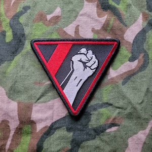 May include: A black and red triangular patch with a white raised fist in the center. The patch has a red stripe across the top and a black stripe across the bottom.