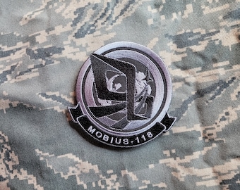 May include: A black and silver embroidered patch with a stylized "M" and the text "MOBIUS-118".