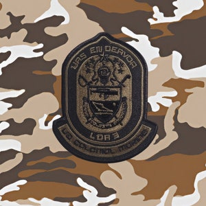 May include: A black and gold embroidered patch with the text "LAS EN DEAVOR L.D.R. 3 LA COLONIAL MARINE" in a circular design.