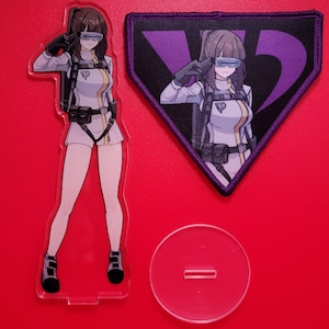 May include: A clear acrylic stand featuring an anime character in a white jumpsuit and goggles. The character is saluting with her right hand. The stand is set against a red background. A purple and black patch with a stylized letter V is also visible.