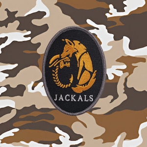 Pode incluir: Um remendo bordado preto e dourado com um chacal e a palavra "JACKALS" em texto branco.