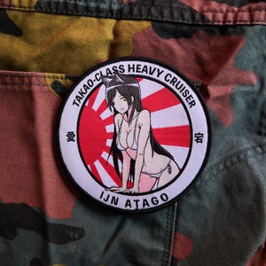 May include: A circular patch with an anime-style illustration of a woman in a bikini, set against a red and white rising sun design. Text includes "TAKAO-CLASS HEAVY CRUISER" and "IJN ATAGO". The patch is on a camouflage background.