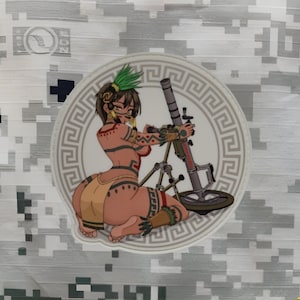 May include: A white circle with a gray Greek key border surrounds a colorful illustration of a woman in a tribal outfit holding a mortar. The woman is wearing a brown and yellow skirt, a red and black top, and a green headdress. The mortar is gray and black with a red handle.