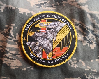 May include: A black and yellow embroidered patch with a fighter jet and the text "156th Tactical Fighter Wing Yellow Squadron SU-37 Terminator".