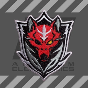 Puede incluir: Parche bordado con un diseño de cabeza de lobo rojo dentro de un escudo blanco y negro. El lobo tiene un ojo amarillo y detalles grises. El parche está bordeado en blanco y negro, con el texto "A ELE M ICS" en la parte inferior.