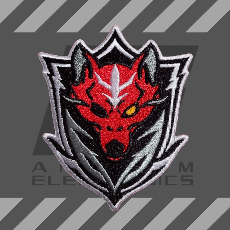 Puede incluir: Parche bordado con un dise&ntilde;o de cabeza de lobo rojo dentro de un escudo blanco y negro. El lobo tiene un ojo amarillo y detalles grises. El parche est&aacute; bordeado en blanco y negro, con el texto "A ELE M ICS" en la parte inferior.