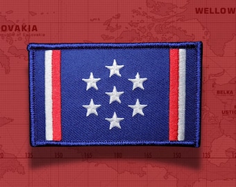 May include: A rectangular embroidered patch featuring a blue field with seven white stars arranged in a circular pattern. The patch includes vertical white and red stripes on both the left and right sides, finished with a dark blue stitched border.