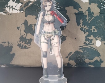May include: A clear acrylic stand-up figure of a female anime character. The character wears a black bikini top, camouflage shorts, and a red arm sleeve. She has an eyepatch and is posed on a clear circular base.