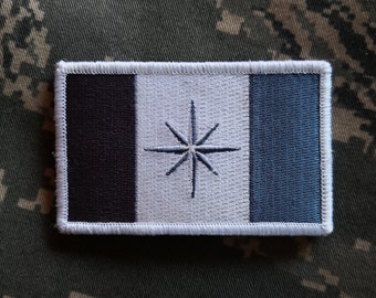 May include: A white patch with a black and blue border. The patch features a white star with eight points in the centre.