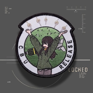 May include: A circular embroidered patch featuring a character with dark hair wearing an olive green sweater, arms raised against a green circular background. The white border contains the text CBU RELEASE and five small golden icons above the character.