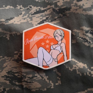 May include: An orange and white embroidered patch with the text "Rosa Cosette D'Elise" and an anime-style illustration of a woman in lingerie. The patch is in a hexagonal shape and features a star design.