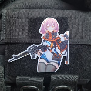May include: A black and white anime-style illustration of a woman holding a rifle. She is wearing a blue and orange outfit with a black jacket. The illustration is printed on a black patch.
