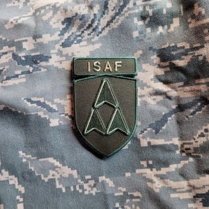 May include: A green and black embroidered patch with the text "ISAF" and a stylized triangle design.