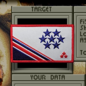 May include: A rectangular embroidered patch featuring a white background with a red border. The design includes a diagonal stripe of dark blue and red, a cluster of seven dark blue stars, and a smaller cluster of three red stars in the corner.
