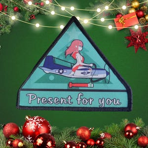 May include: A triangular Christmas patch featuring a cartoon image of a woman in a red swimsuit flying a blue and white aeroplane. The text "Present for you" is printed on the patch.