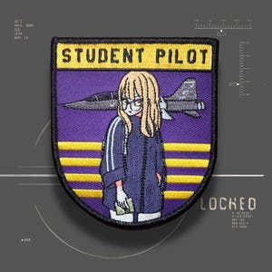 May include: A shield-shaped embroidered patch with a black border, featuring the text "STUDENT PILOT" in black on a yellow background. The design includes a purple field with yellow horizontal stripes, a fighter jet, and a blonde character wearing glasses.