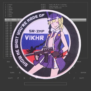 以下が含まれることがあります： ピンクの縁取りのある丸い白いパッチ。パッチには、黒い銃を持った漫画の女性が描かれている。女性は紫色のドレスと白い帽子をかぶっている。パッチの縁には黒い文字で「SHOW ME WHAT YOU'RE MADE OF」と書かれている。パッチの中央には白い文字で「SR-3MP VIKHR」と書かれている。