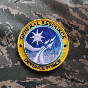 May include: A yellow and blue embroidered patch with the text "General Resource Defence Force" and a white star with two white jets flying upwards.