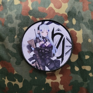 Könnte beinhalten: Ein weißer und schwarzer runder Patch mit einem Cartoon-Bild einer Frau mit blauen Haaren, die ein Gewehr hält. Der Text "DON'T EXIST" befindet sich auf dem Patch.